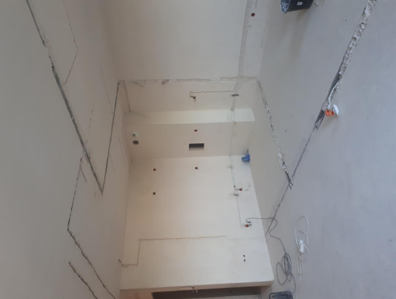 Wnętrze w trakcie remontu z wyżłobieniami w ścianach pod instalację elektryczną, widoczne przewody i puszki elektryczne, surowy stan wykończenia ścian.