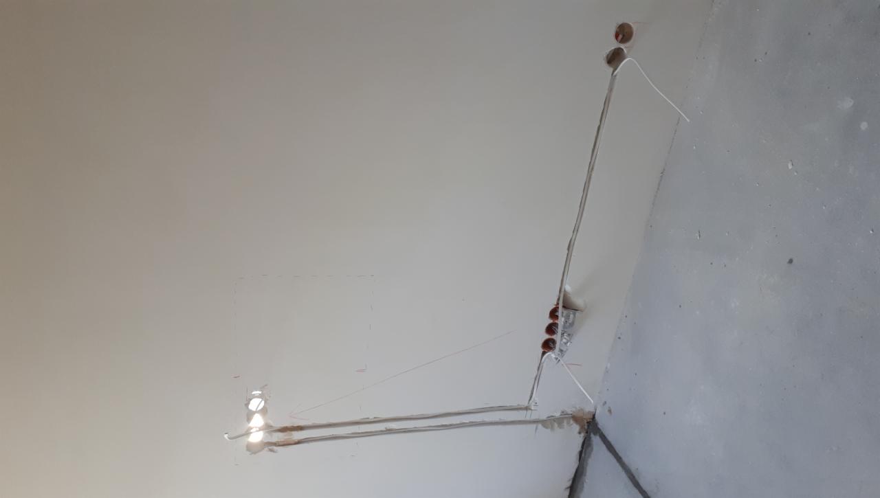 Fragment ściany w trakcie prac elektrycznych: widoczne kable w bruzdach, puszki instalacyjne oraz otwory na gniazdka, przygotowane do dalszego montażu.