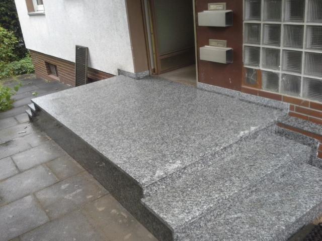 Granitowe schody wejściowe i podest przed budynkiem, widoczne skrzynki na listy i okno z luksferów.