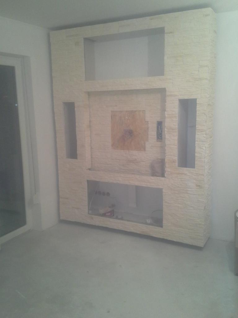 Ściana telewizyjna w trakcie wykańczania, obłożona dekoracyjnym kamieniem w Namysłowie, z widocznymi otworami na sprzęt RTV i elementami instalacji elektrycznej.