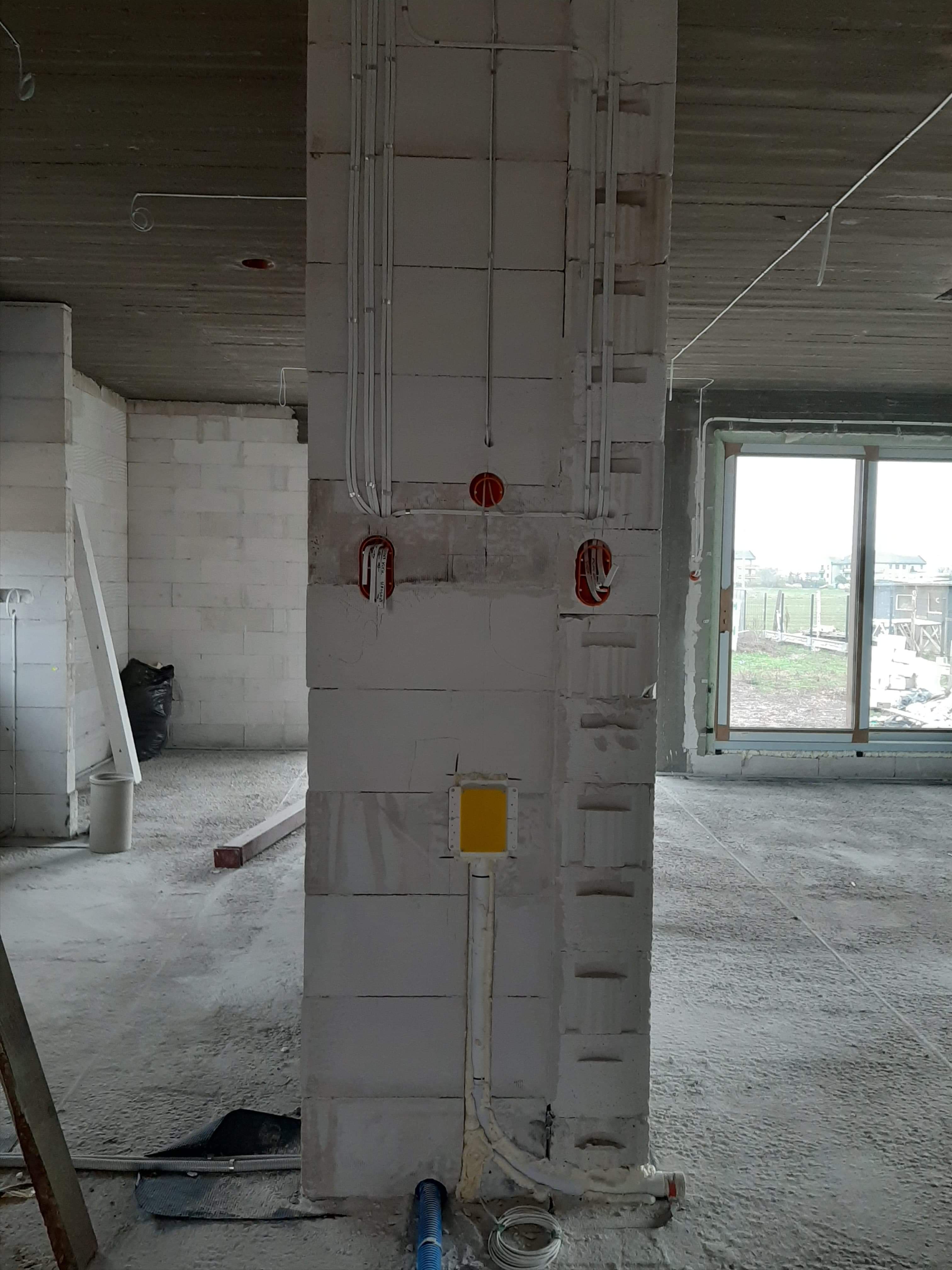 Wewnętrzna instalacja elektryczna w surowym stanie: widoczne przewody w peszlach, puszki instalacyjne w ścianie z betonu komórkowego, przygotowanie do montażu gniazdek i włączników.