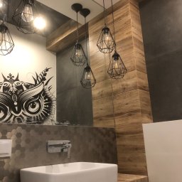 N2C - Nowoczesna łazienka z umywalką nablatową, heksagonalnymi płytkami, drewnopodobną okładziną ścienną i wiszącymi lampami w kształcie klatek, z odbiciem grafiki sowy w lustrze.