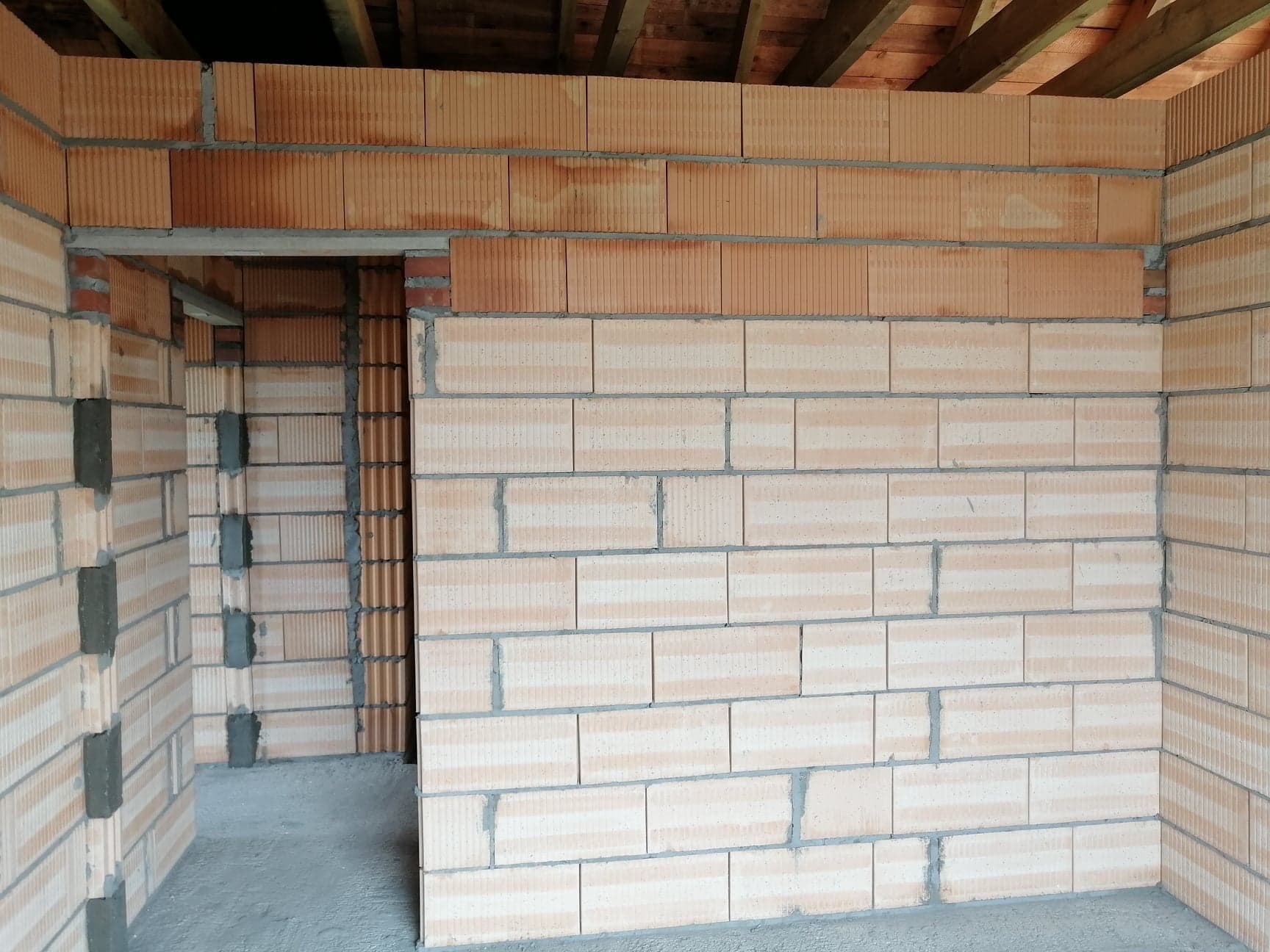 Wnętrze domu w trakcie budowy, ściany wzniesione z bloczków ceramicznych, widoczne drewniane elementy konstrukcji dachu.