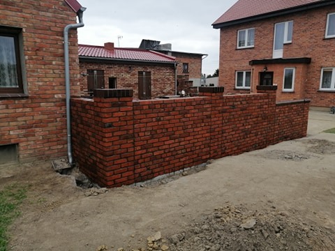 Nowo wybudowany, niski murek z czerwonej cegły, otaczający część domu z cegły, widoczny fragment rynny spustowej.