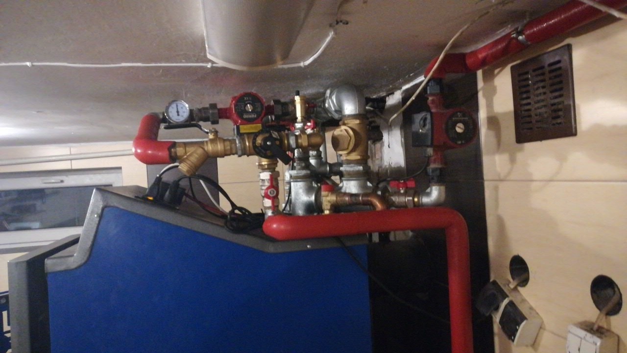 Węzeł cieplny z rurami w kolorze czerwonym i mosiężnymi zaworami, manometr na rurze, widoczne pompy obiegowe, zamontowany w pomieszczeniu technicznym.