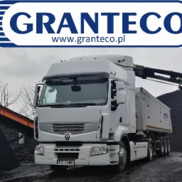 Biała ciężarówka z naczepą na tle hałdy ciemnego materiału i podajnika taśmowego, logo firmy na górze zdjęcia.