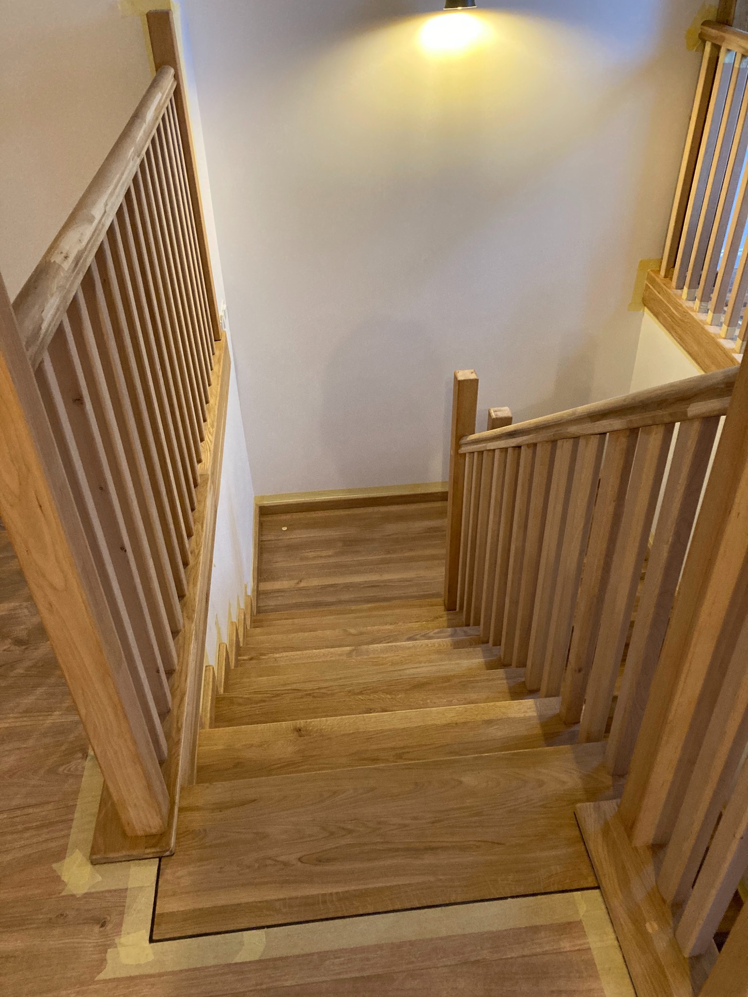 Drewniane schody z balustradą w trakcie montażu, zabezpieczone taśmą malarską, widok z góry na dół.
