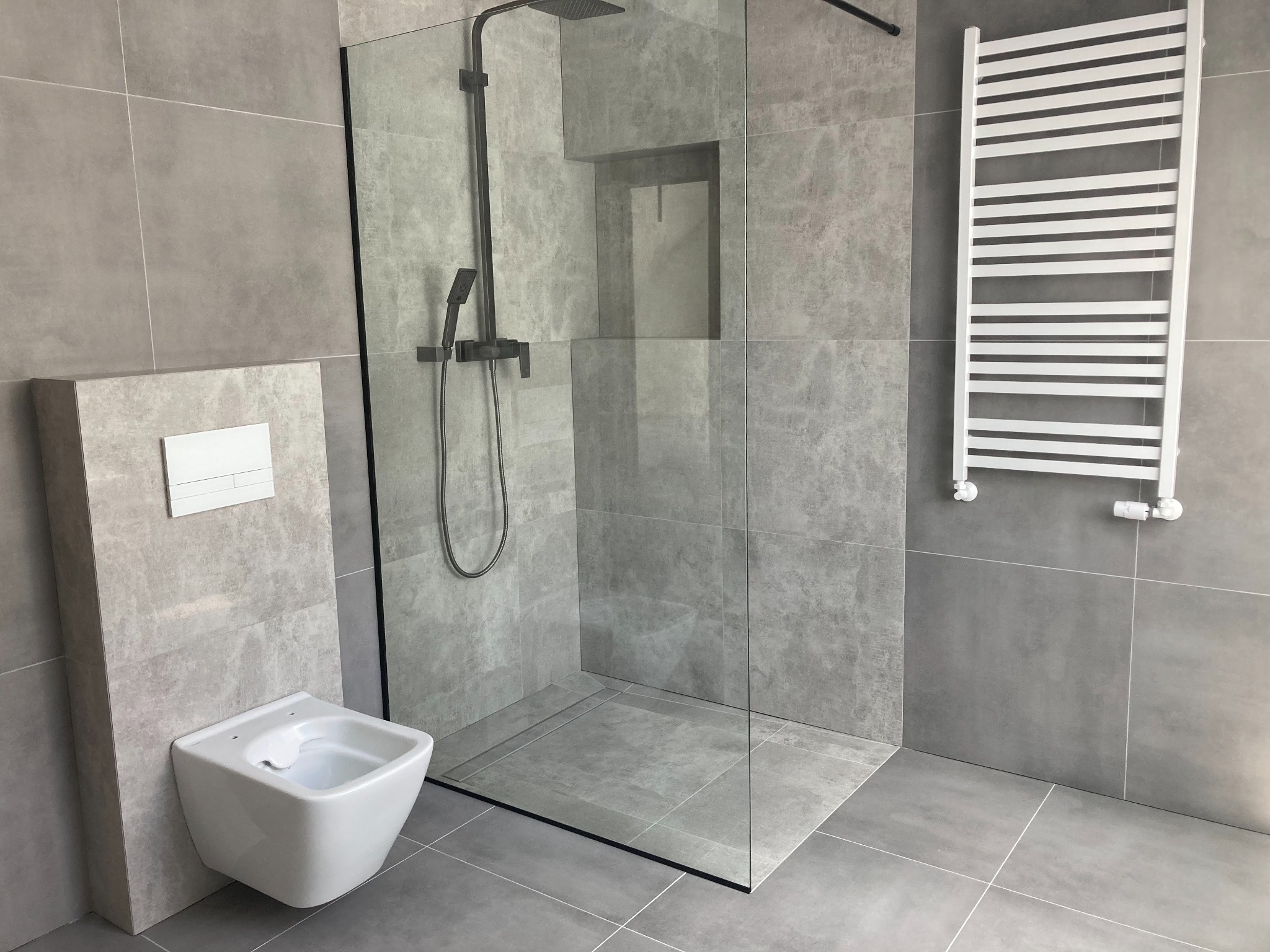 Nowoczesna łazienka wykończona w odcieniach szarości z kabiną prysznicową typu walk-in, podwieszanym bidetem i grzejnikiem drabinkowym.