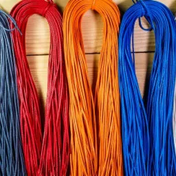 Sznurki sk&oacute;rzane w kolorach: szarym, czerwonym, pomarańczowym, niebieskim i białym, ułożone obok siebie na drewnianym tle.