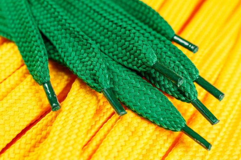Makro ujęcie zielonych sznurówek na tle żółtych, ukazujące detale splotu i plastikowe końcówki.