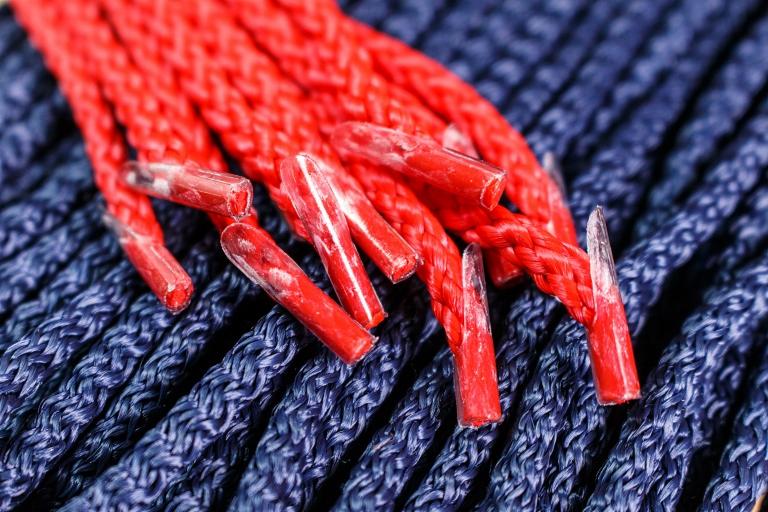 Makro ujęcie czerwonych sznurówek z plastikowymi końcówkami na tle niebieskiej plecionej liny.
