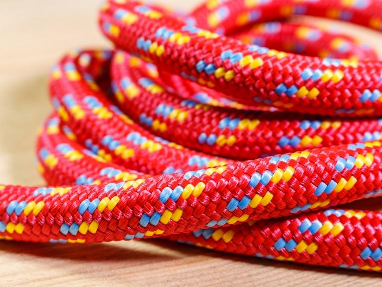 Zwój czerwonej, plecionej liny z niebieskimi i żółtymi akcentami na drewnianej powierzchni, ukazujący szczegółowy splot i teksturę.