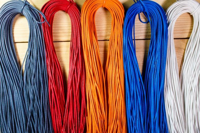 Sznurki skórzane w kolorach: szarym, czerwonym, pomarańczowym, niebieskim i białym, ułożone obok siebie na drewnianym tle.