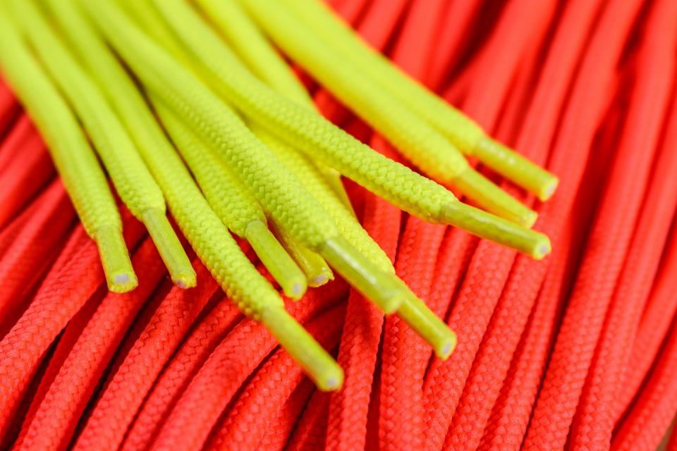 Jaskrawożółte sznurówki na tle zwiniętej czerwonej liny, zbliżenie na końcówki sznurówek i teksturę liny.