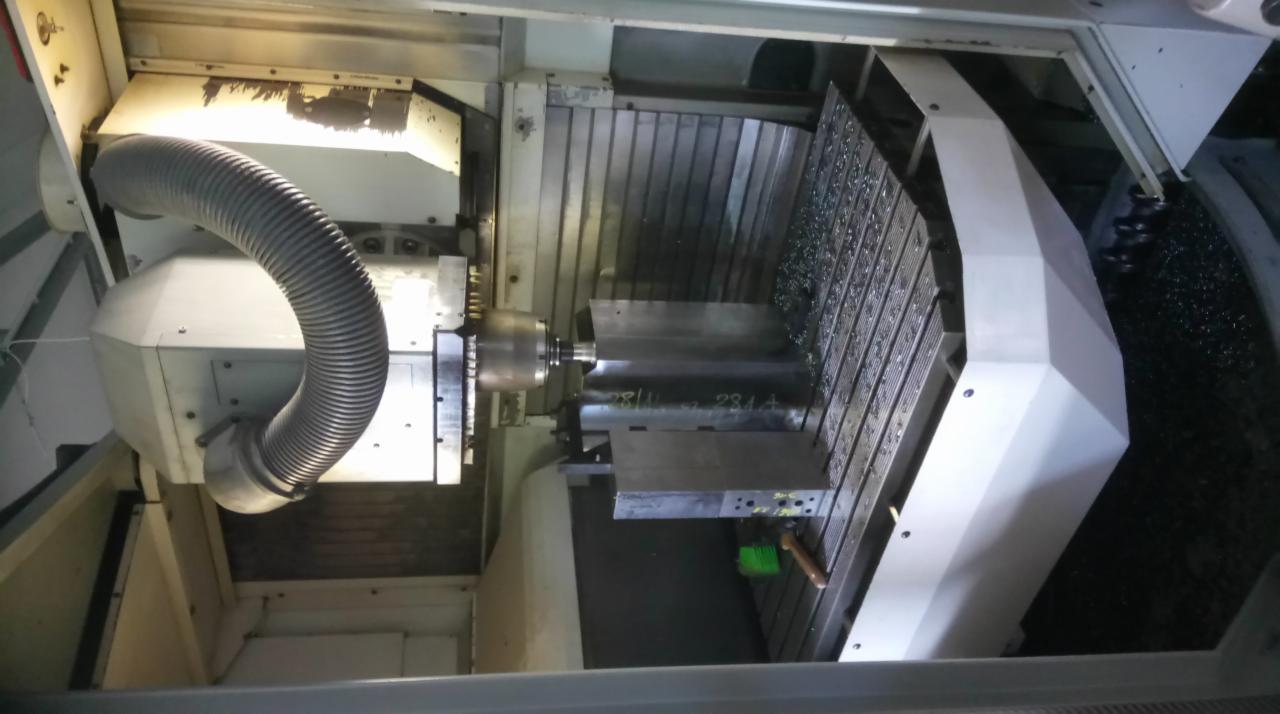 Wnętrze maszyny CNC z obrabianym metalowym elementem, widoczne wióry i narzędzia skrawające.