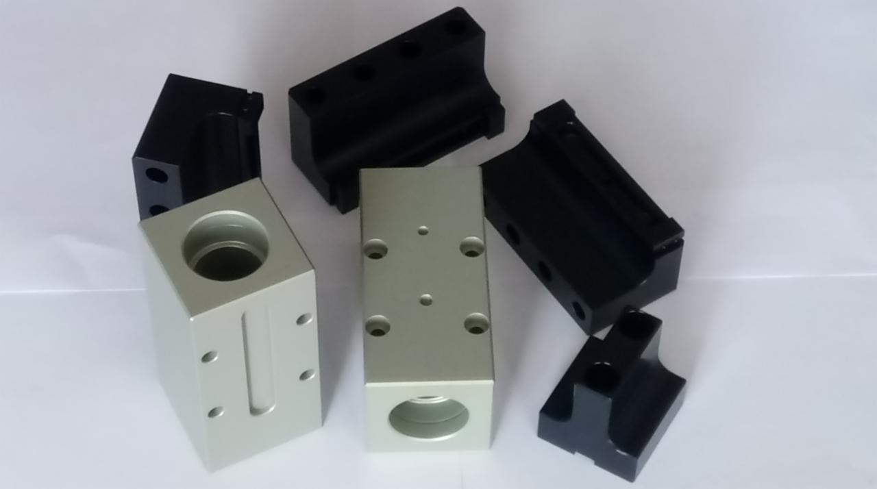 Precyzyjnie obrobione, srebrne i czarne metalowe elementy z otworami, leżące na białym tle. Widoczne ślady obróbki.