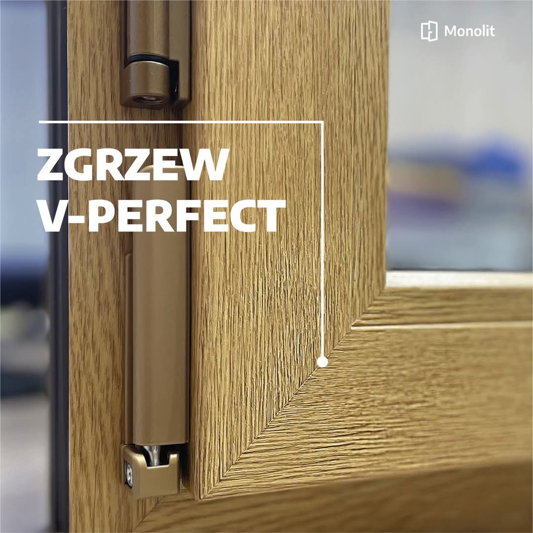 Szczegółowy widok narożnika okna z profilem w kolorze jasnego dębu, z widocznym okuciem i precyzyjnym łączeniem ramki, podkreślonym napisem 'ZGRZEW V-PERFECT'.