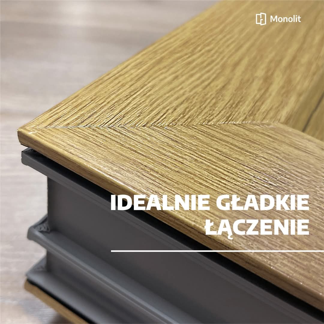 Szczegółowe zbliżenie na narożnik ramy okiennej z efektem drewna i idealnie gładkim połączeniem, szara podstawa ramy, widoczne logo producenta w prawym górnym rogu.