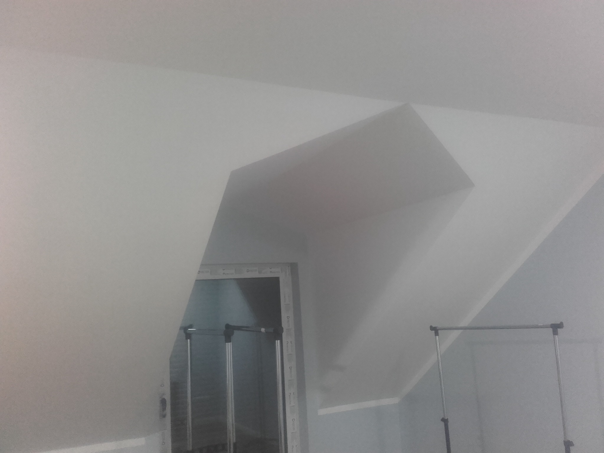 Poddasze po remoncie z pomalowanymi na biało ścianami i sufitem, widoczny fragment garderoby z metalowym wieszakiem na ubrania.