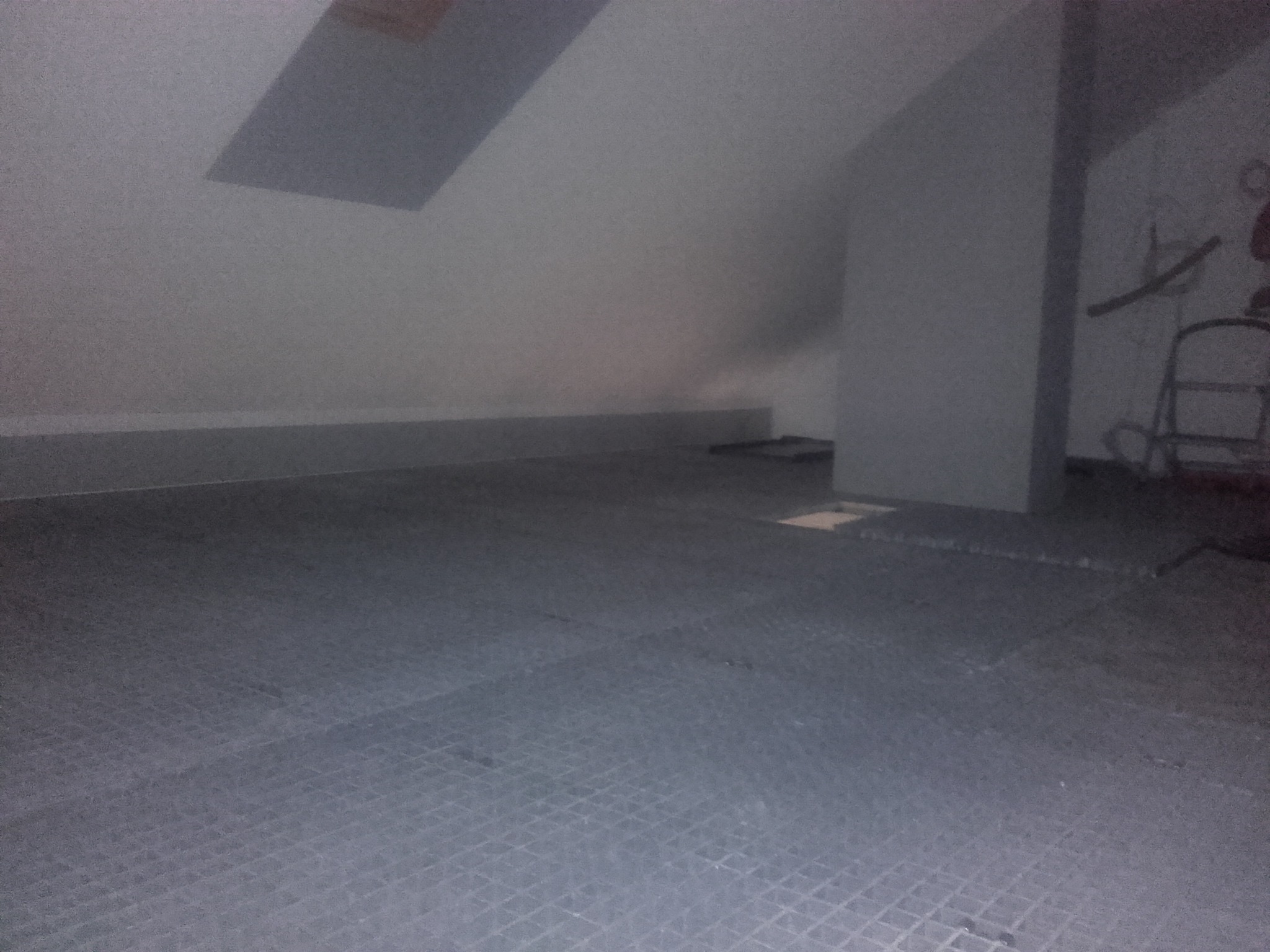 Podłoga w szarych płytach w trakcie prac w poddaszowym pomieszczeniu ze skosem i oknem dachowym, widoczna drabina i ślady po instalacjach.