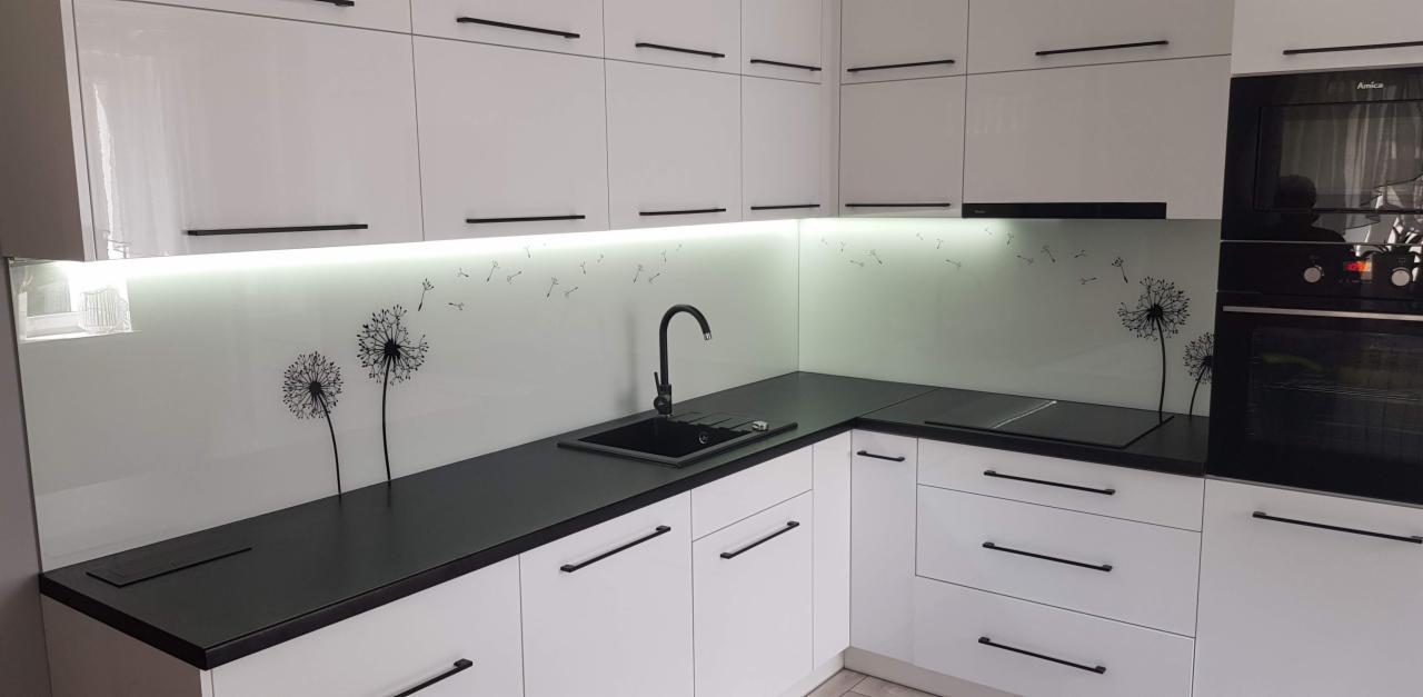 Biała kuchnia z czarnym blatem i szklanym panelem ściennym z motywem dmuchawca podświetlonym od spodu