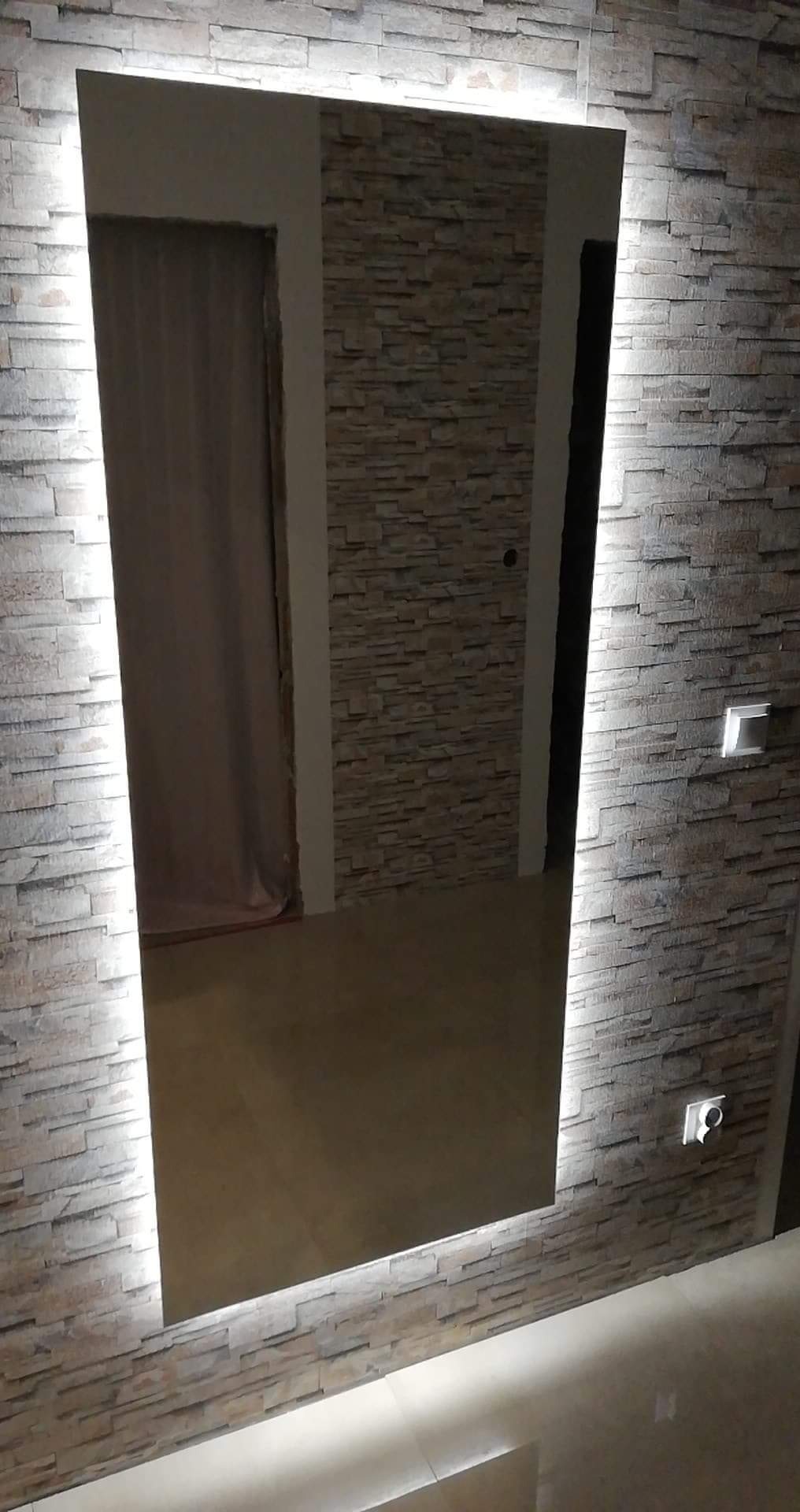 Prostokątne lustro z podświetleniem LED wbudowane w ścianę z dekoracyjnej cegły, odbijające wnętrze pokoju.