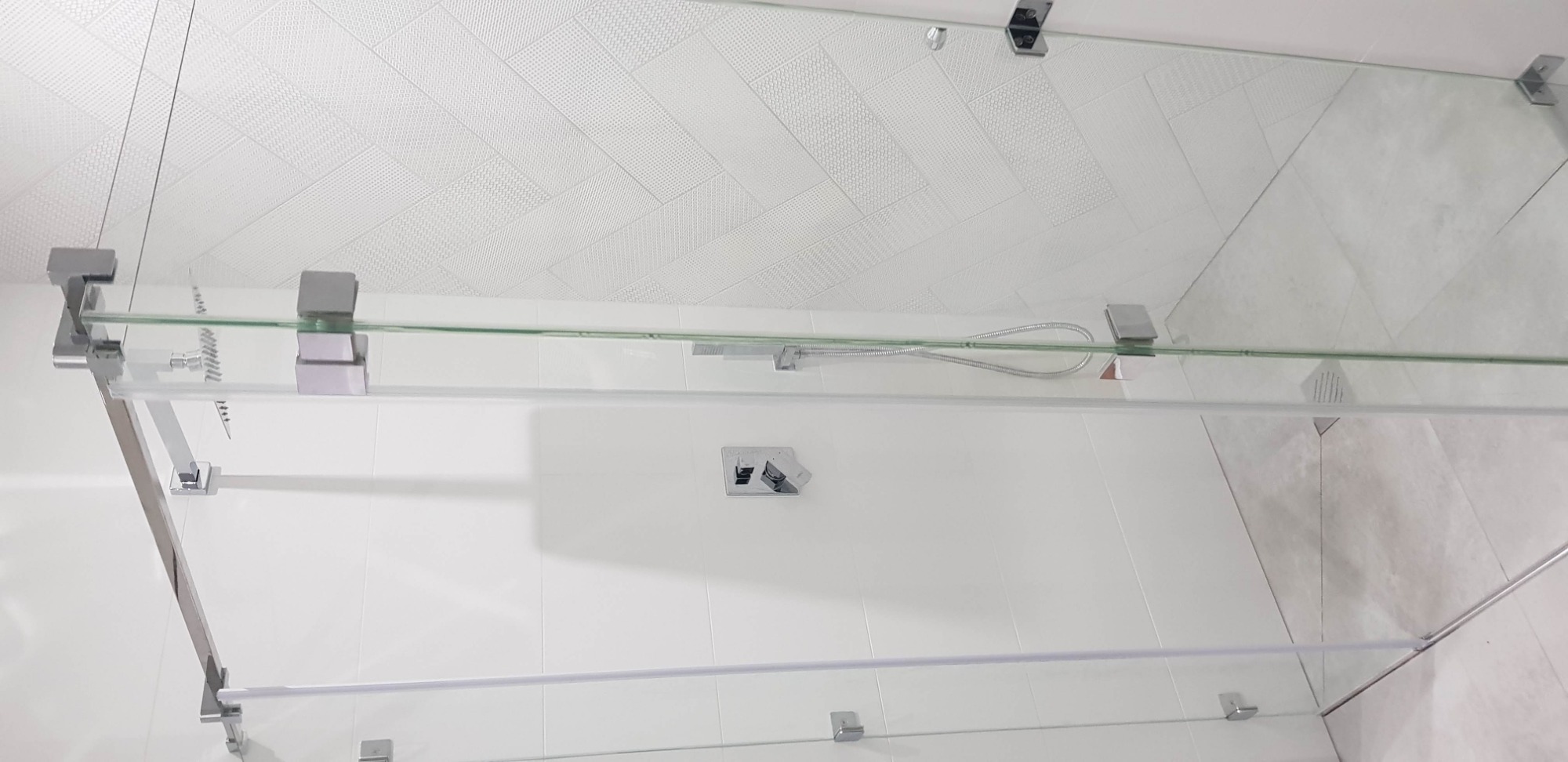 Szklana kabina prysznicowa z chromowanymi okuciami, widok od góry, białe płytki na ścianach i suficie.