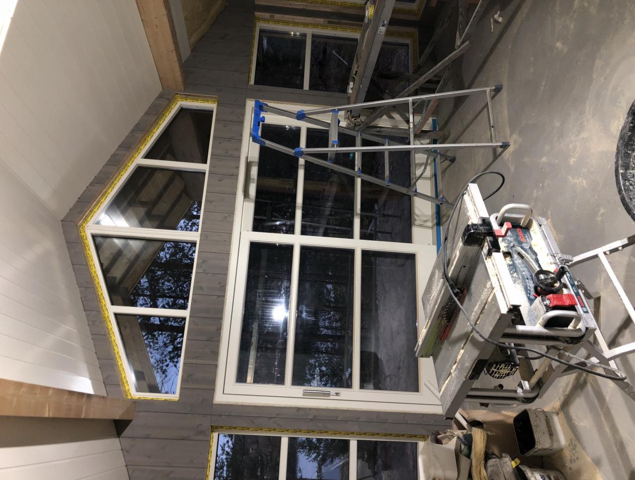 Montaż okien w nowym domu z drewnianą boazerią, widoczne narzędzia i drabina.