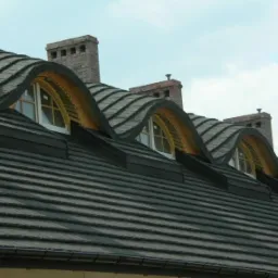 Czarny dach z dach&oacute;wki ceramicznej z trzema p&oacute;łokrągłymi oknami lukarn i trzema kominami z cegły.