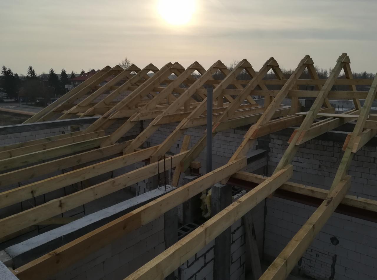 Konstrukcja więźby dachowej z drewna na murach z białej cegły silikatowej w trakcie budowy domu, widok z góry przy zachodzącym słońcu.