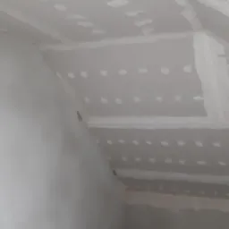 Poddasze w trakcie szpachlowania: widoczne płyty gipsowo-kartonowe na skosach sufitu i ścianach z zaszpachlowanymi łączeniami i śrubami, przygotowane do dalszych prac wykończeniowych.