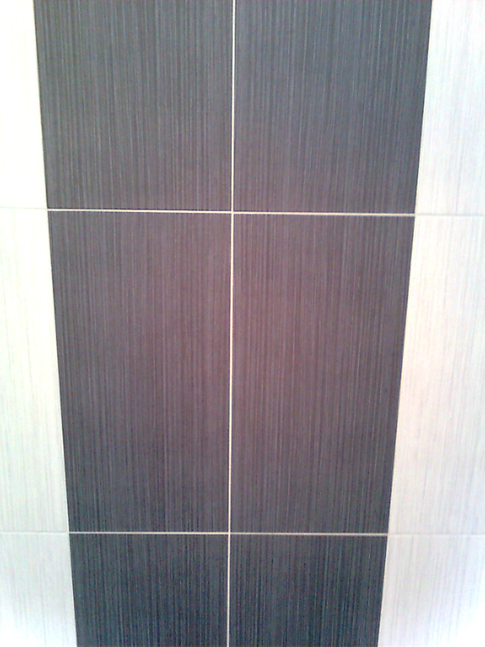 Układ płytek ściennych w odcieniach szarości i bieli, z widocznymi fugami krzyżowymi, tworzących geometryczny wzór.