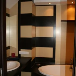 Wykończona łazienka z umywalką i wanną, ściany wyłożone płytkami w poziome pasy beżu i czerni, oświetlenie punktowe sufitowe, czarny blat i obudowa wanny z mozaiki.