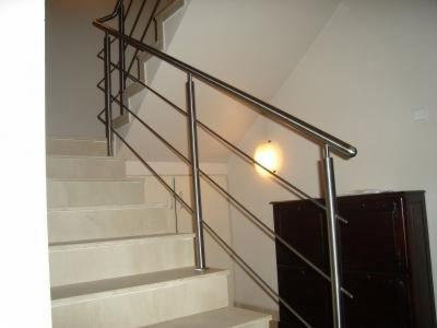 Nowoczesna balustrada nierdzewna ze stali szczotkowanej, zamontowana przy marmurowych schodach. Ujęcie z dołu, widoczna szafka w tle i oświetlenie.