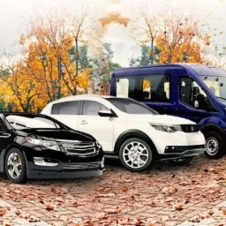 Trzy pojazdy: czarny sedan, biały SUV i niebieski van, ustawione na tle jesiennego parku z opadającymi liśćmi.