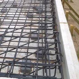 Zakład Ogólnobudowlany Michał Tomalak TOM-MAX - Zbrojenie fundamentów w szalunku z białego styropianu. Widoczne pręty zbrojeniowe ułożone w kratę i pomarańczowe rury instalacyjne. Drewniane podpory szalunku.