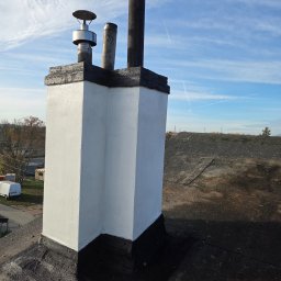 Zakład Ogólnobudowlany Michał Tomalak TOM-MAX - Biały, odnowiony komin na dachu pokrytym papą, z widocznymi elementami wentylacyjnymi i fragmentem nieba z chmurami. Komin pomalowany na biało, z czarnym wykończeniem.