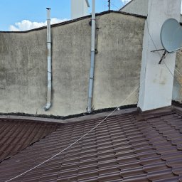 Zakład Ogólnobudowlany Michał Tomalak TOM-MAX - Brązowy dach z blachy trapezowej na tle szarej ściany budynku z kominami i anteną satelitarną. Widok z góry, w słoneczny dzień.