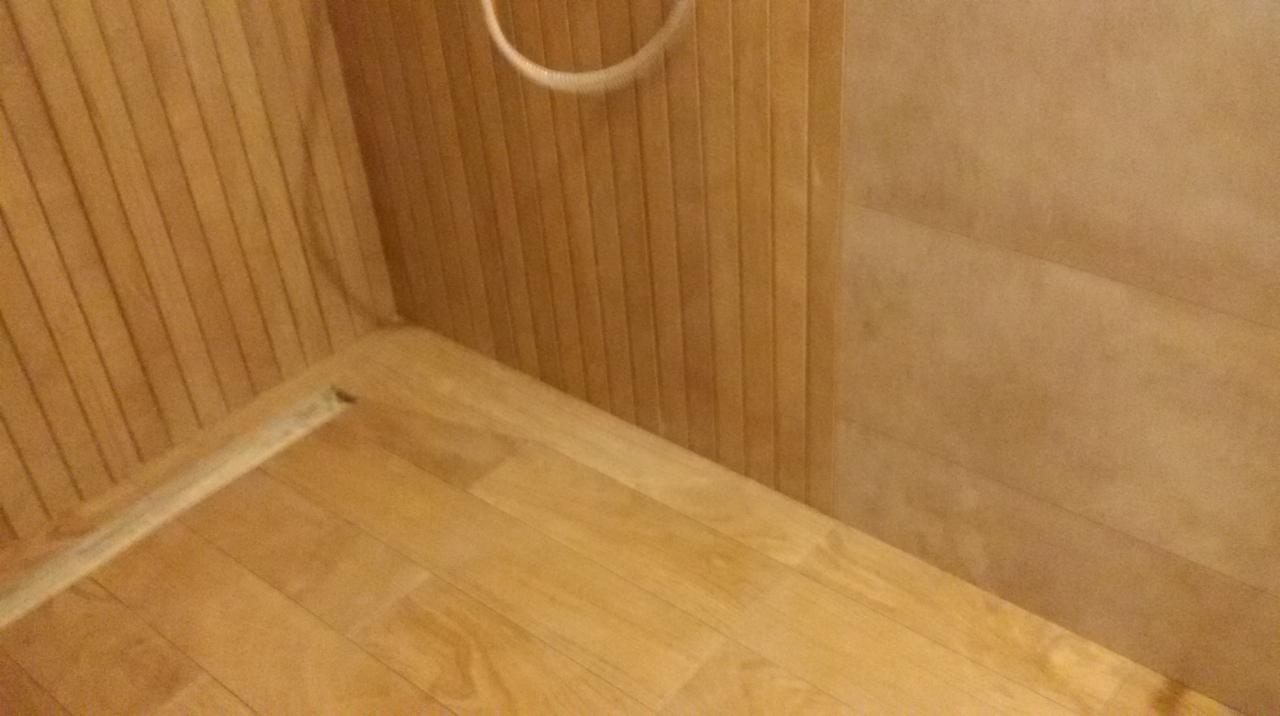 Fragment wykończonej łazienki z drewnianą podłogą i panelami ściennymi w odcieniach beżu i brązu, widoczny uchwyt na ręcznik.