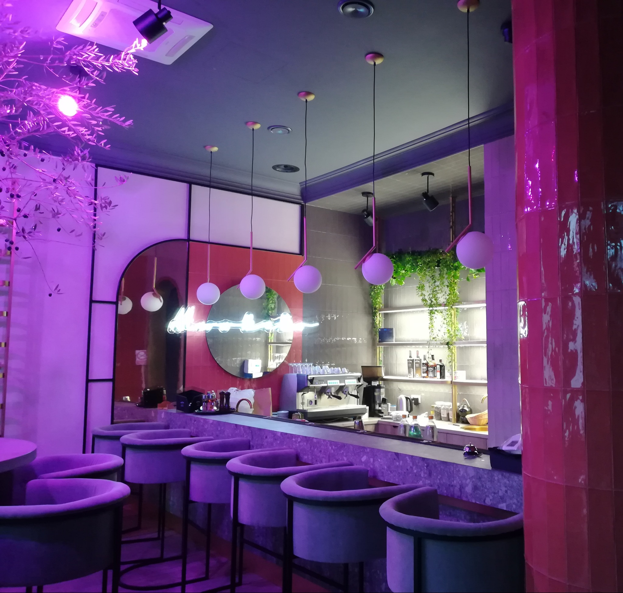 Nowoczesny bar z fioletowym oświetleniem, okrągłe lustro z neonem, designerskie krzesła barowe i różowe płytki na filarze. Wykończenie wnętrza lokalu.