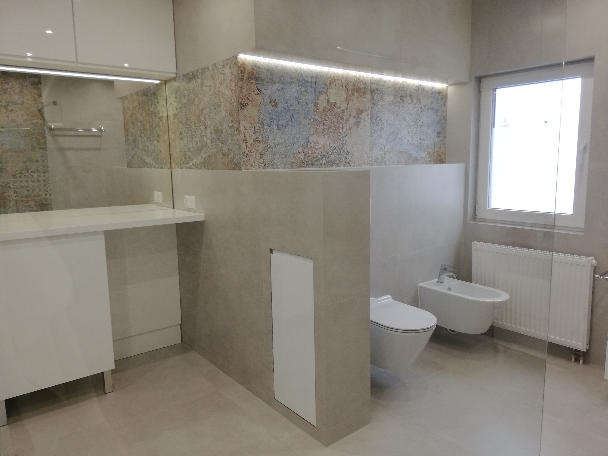 Nowoczesna łazienka z umywalką, toaletą i bidetem w odcieniach beżu i bieli. Dekoracyjna ściana z oświetleniem LED. Minimalistyczny design.