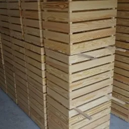 Stosy świeżo wyprodukowanych, jasnych, drewnianych skrzynek z listew, ułożonych w magazynie, widoczne naturalne usłojenie drewna.
