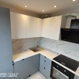 Nowoczesna kuchnia w odcieniach szarości i bieli z marmurowym blatem, zrealizowana w Kaliszu. Widoczny zlew, płyta indukcyjna i czarny okap.