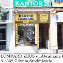 Fasada kantoru Lombard Zeus w Gdyni, z szyldami informującymi o pożyczkach pod zastaw i skupie złota, widok z zewnątrz, lekko pochmurne oświetlenie.