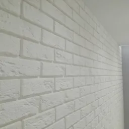 Biała ściana wyłożona dekoracyjnymi płytkami imitującymi cegłę, widok pod kątem, oświetlenie sufitowe.