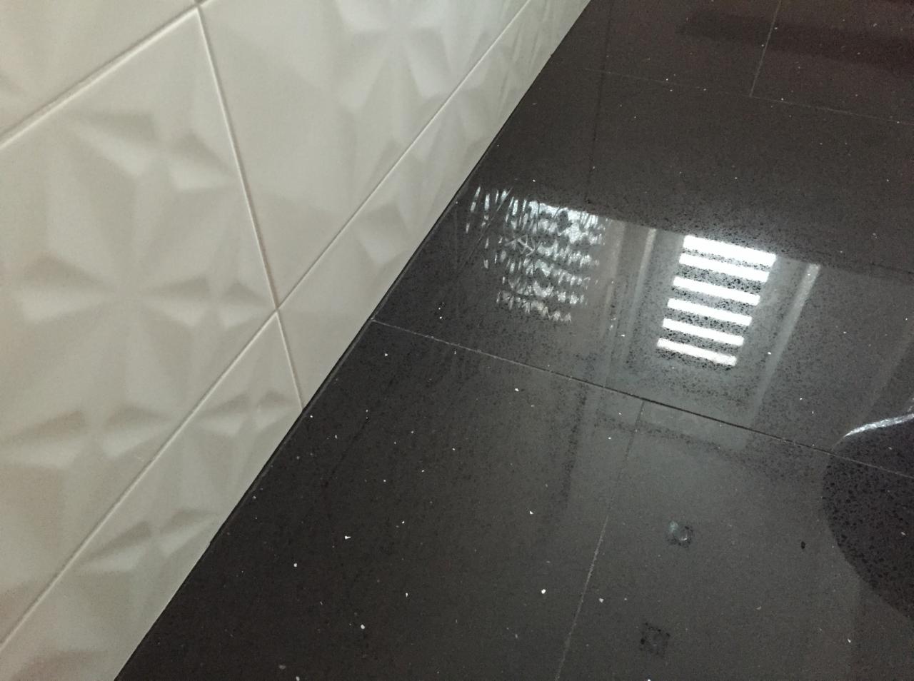 Błyszcząca, czarna podłoga z płytek z białymi drobinkami, odbijająca światło okna, sąsiadująca z białą ścianą z trójwymiarowych płytek.