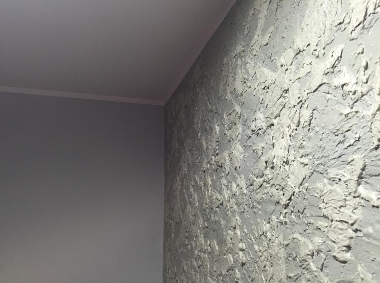 Szara ściana wewnętrzna z dekoracyjną, strukturalną fakturą, widoczny narożnik pomieszczenia i fragment gładkiego sufitu z listwą.
