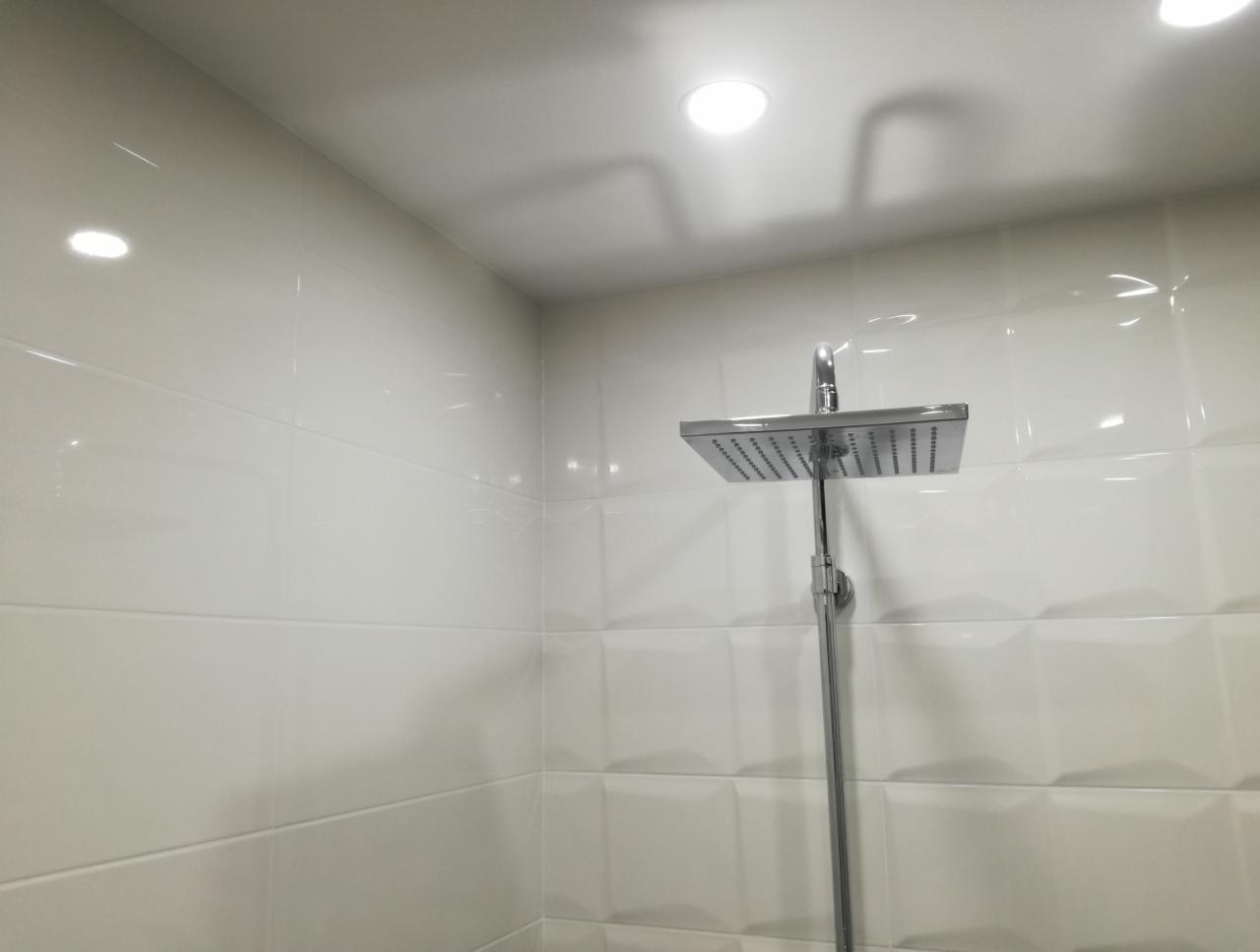 Nowoczesna kabina prysznicowa z kwadratową deszczownicą i białymi, błyszczącymi płytkami ułożonymi w cegiełkę z delikatnym efektem 3D.