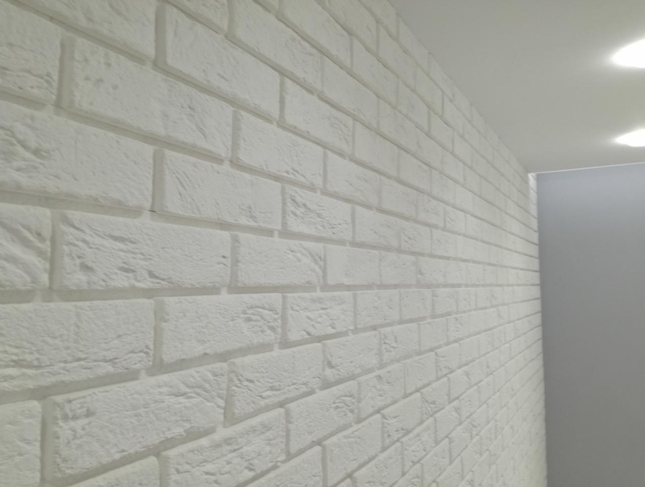 Biała ściana wyłożona dekoracyjnymi płytkami imitującymi cegłę, widok pod kątem, oświetlenie sufitowe.