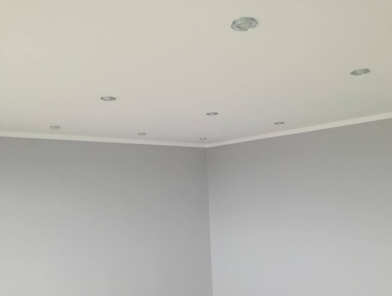 Wnętrze pokoju po remoncie: szare ściany, biały sufit z zamontowanymi punktowymi lampami i listwą dekoracyjną przy ścianie.